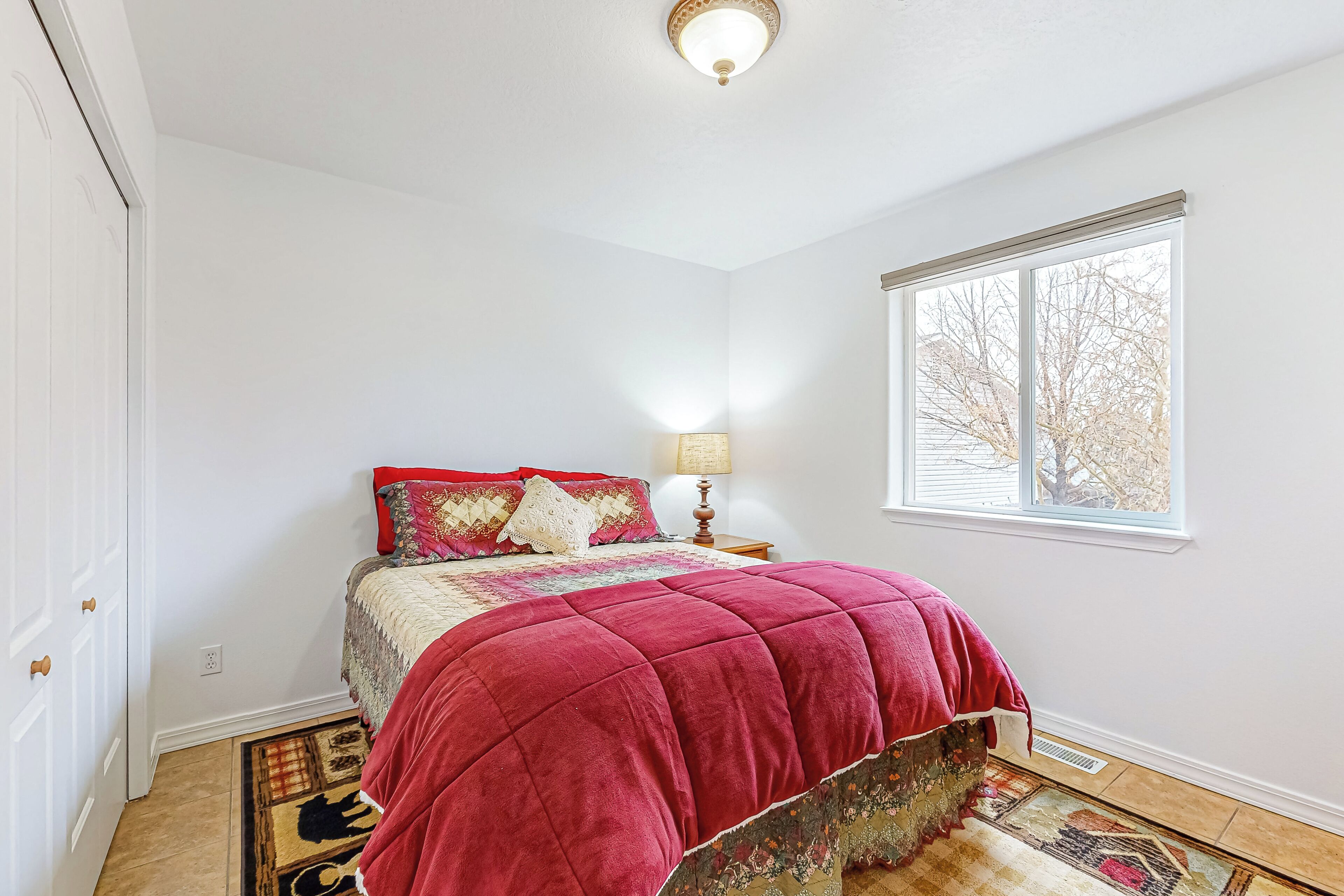 A bedroom with a bed, a window, a lamp, and a door.