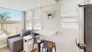A compact kitchen with a white countertop, two bar stools, a grey sofa, and a window with blinds. - Pool & Hot Tub Access: Cozy Perris Tiny Home (Perris)