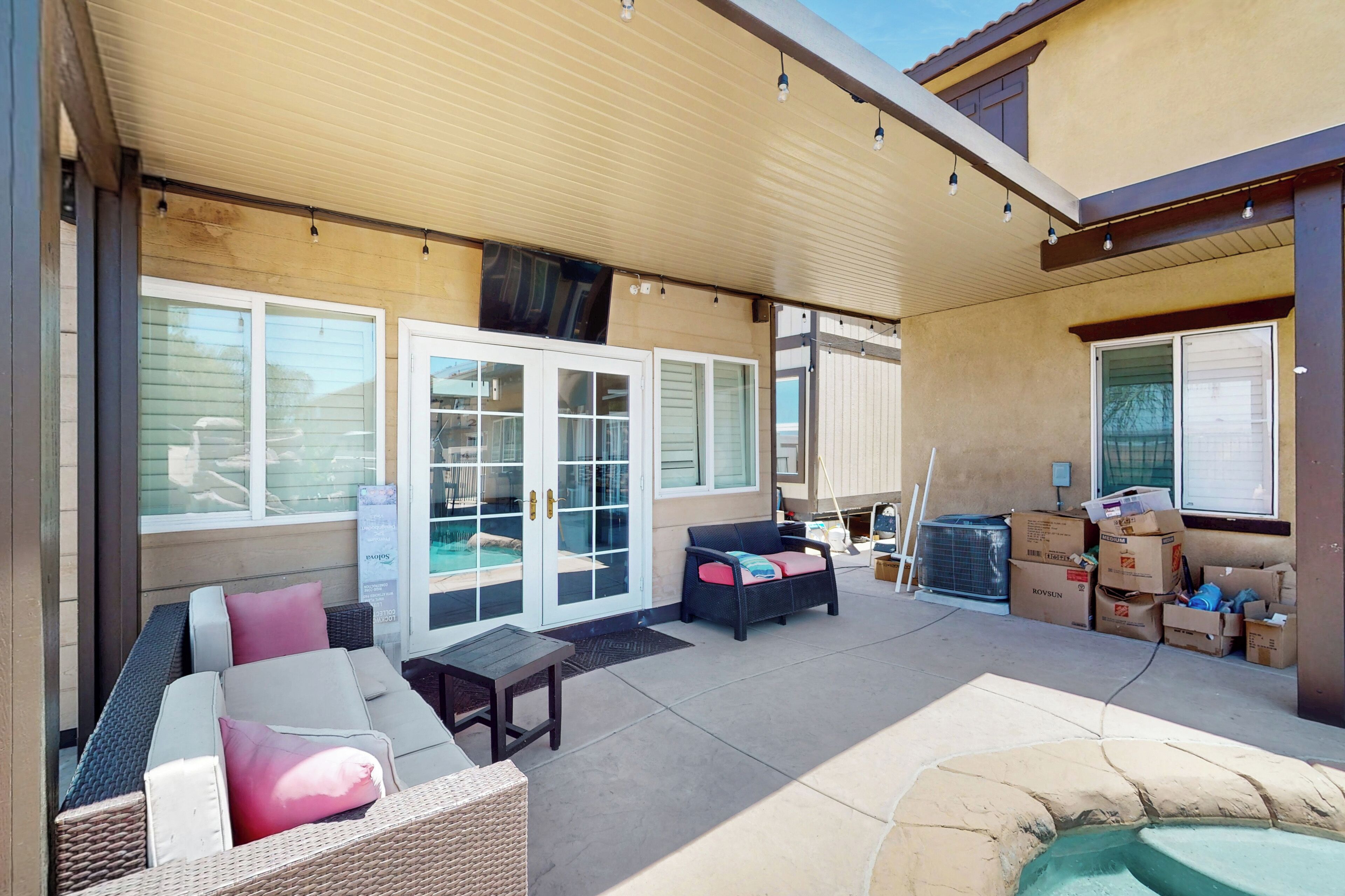 An outdoor patio area with a covered seating area, a fire pit, and a poolside view.