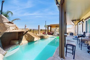 Un área de piscina con una formación rocosa, sillas de descanso y un porche cubierto.
