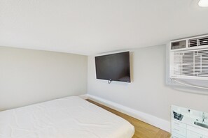 Quarto com cama, TV fixada na parede e aparelho de ar condicionado.