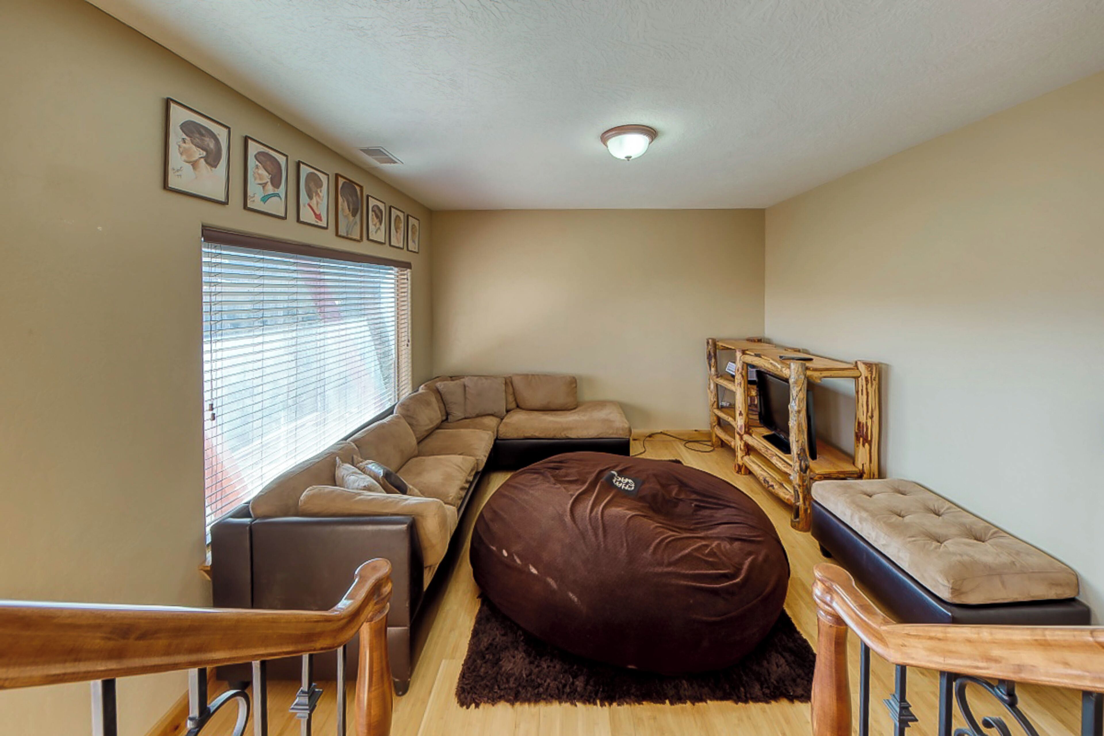 A living room with a sectional sofa, a brown bean bag, a wooden coffee table, and a television on a wooden stand.