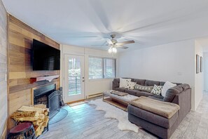 A living room with a fireplace, wooden wall paneling, a gray sofa, and a ceiling fan. - Giant Steps #38 Condo in Brian Head (Brian Head)