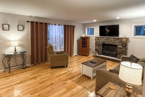A living room with a stone fireplace, a television mounted above it, a sofa, a coffee table, and a chair. - Fire Pit, Game Room, Lake, On-site Stream Poconos! (Blakeslee)