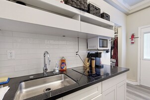 Una cocina moderna con encimera negra, pileta de acero inoxidable, muebles blancos, microondas y extintor.