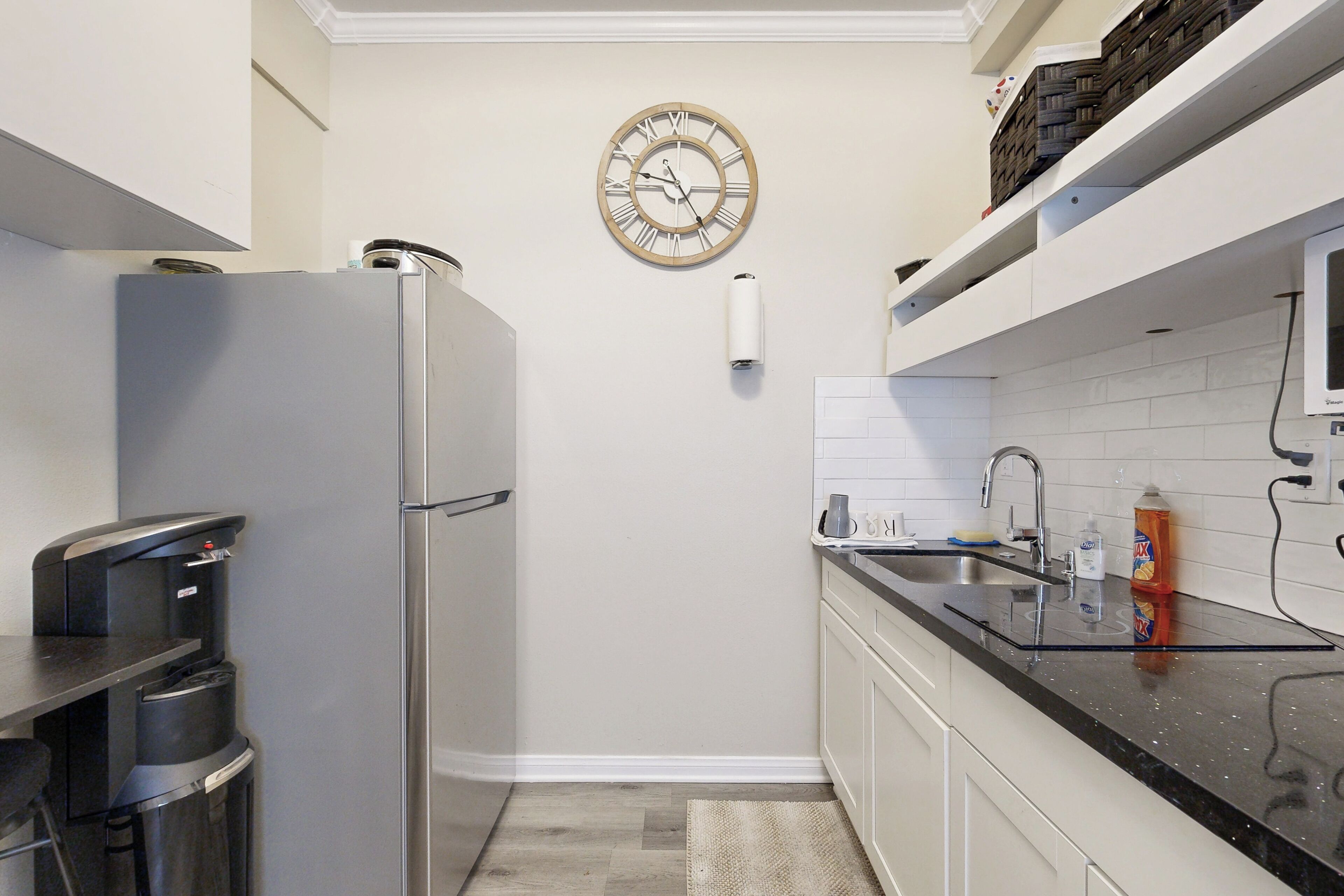 A compact kitchen with a stainless steel refrigerator, a sink, and a clock on the wall.