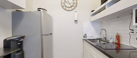 A compact kitchen with a stainless steel refrigerator, a sink, and a clock on the wall.