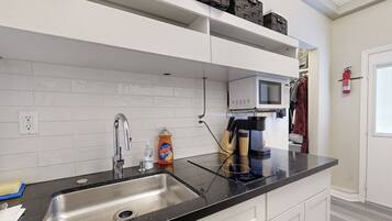Una cocina moderna con encimera negra, pileta de acero inoxidable, muebles blancos, microondas y extintor.