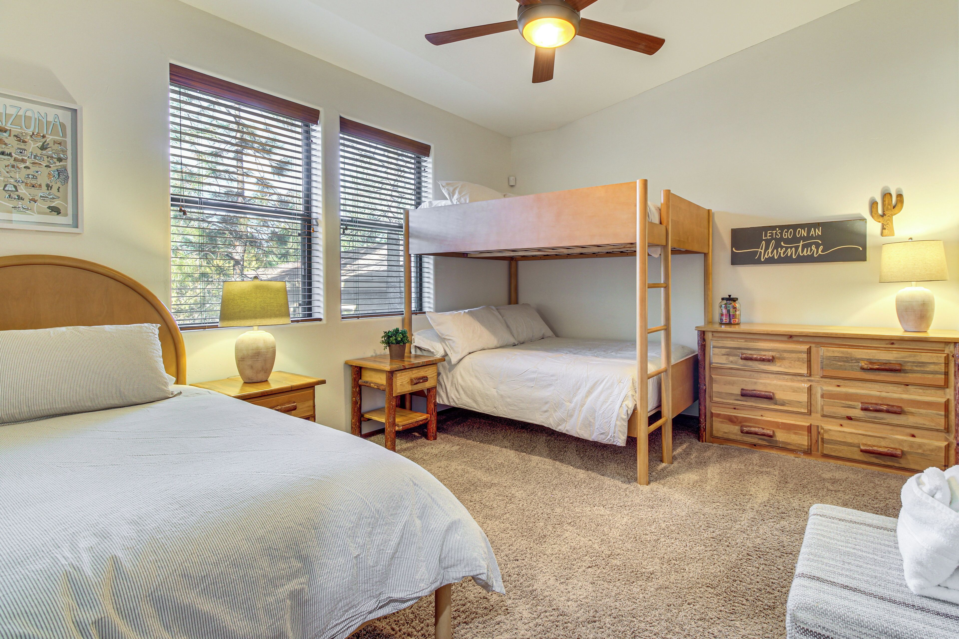 A bedroom with bunk beds, a wooden dresser, a ceiling fan, and a window with blinds.