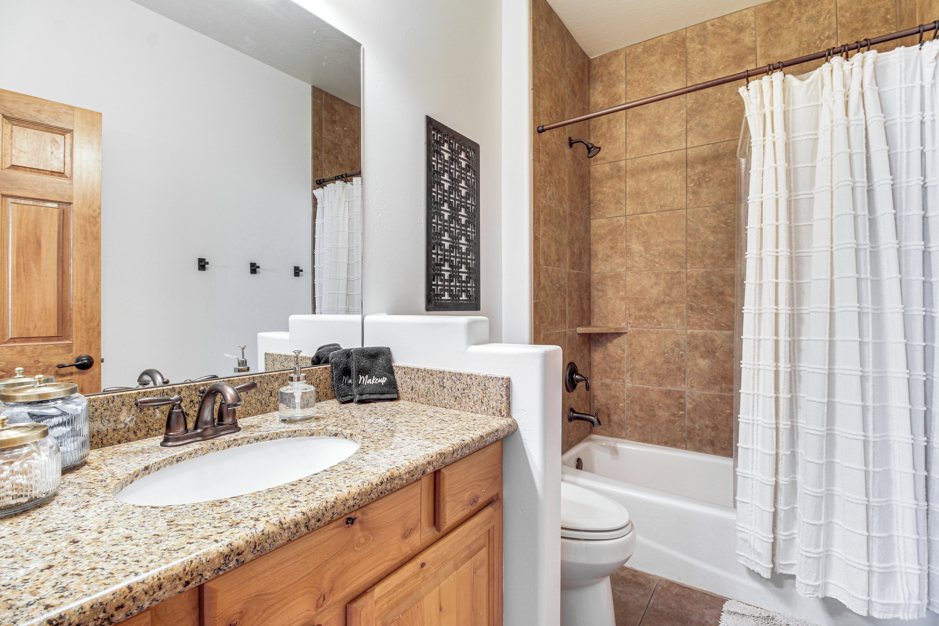 Un baño con encimera de granito, tocador de madera, lavabo blanco, espejo, cortina de ducha y bañera.