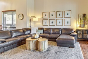 A modern living room with a sectional sofa, two wooden side tables, a round coffee table, and framed pictures on the wall. - 3BR Home w/ Hot Tub, Grill & Wraparound Deck (Show Low)