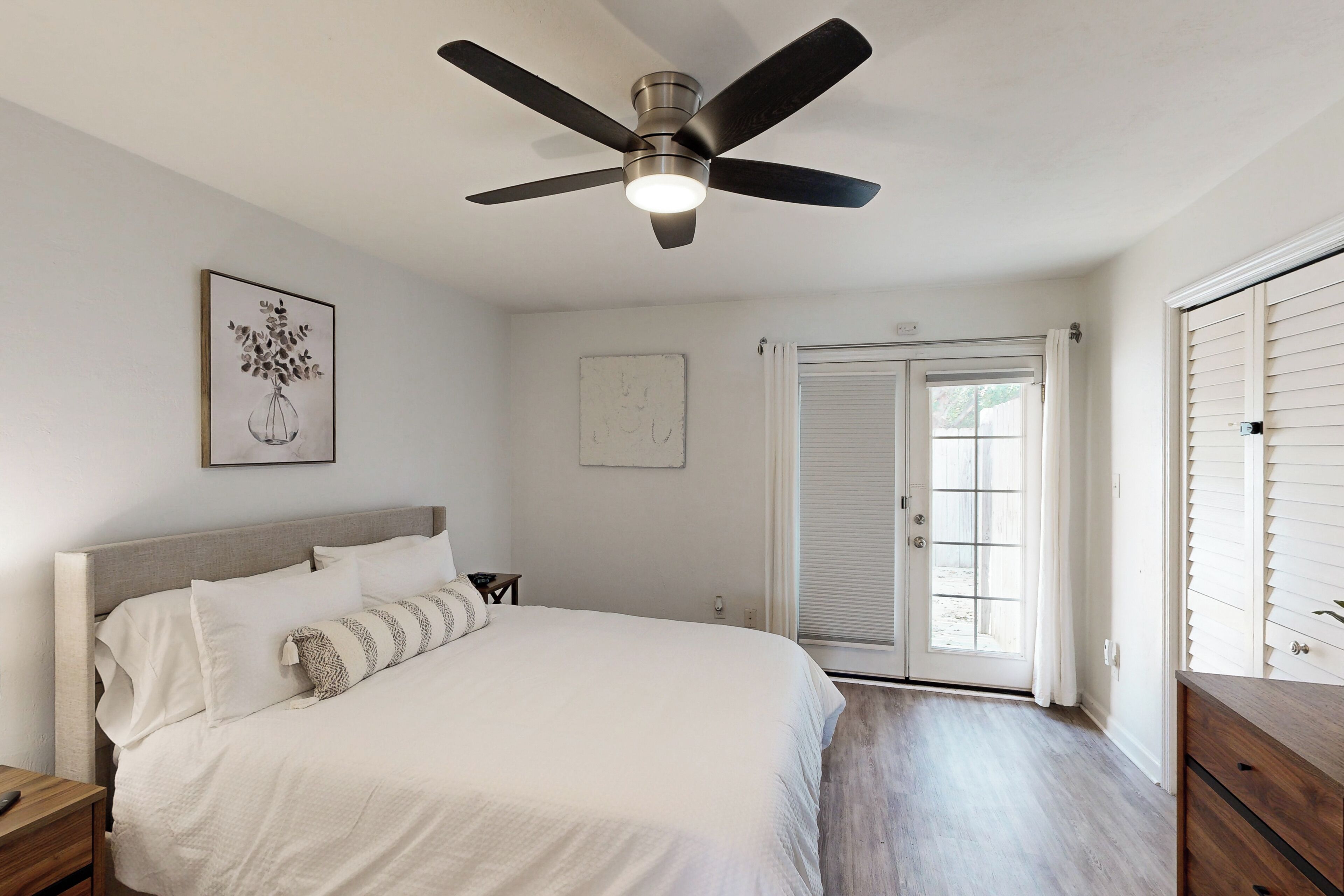 A bedroom with a bed, a ceiling fan, a nightstand, a dresser, and a door with a window.