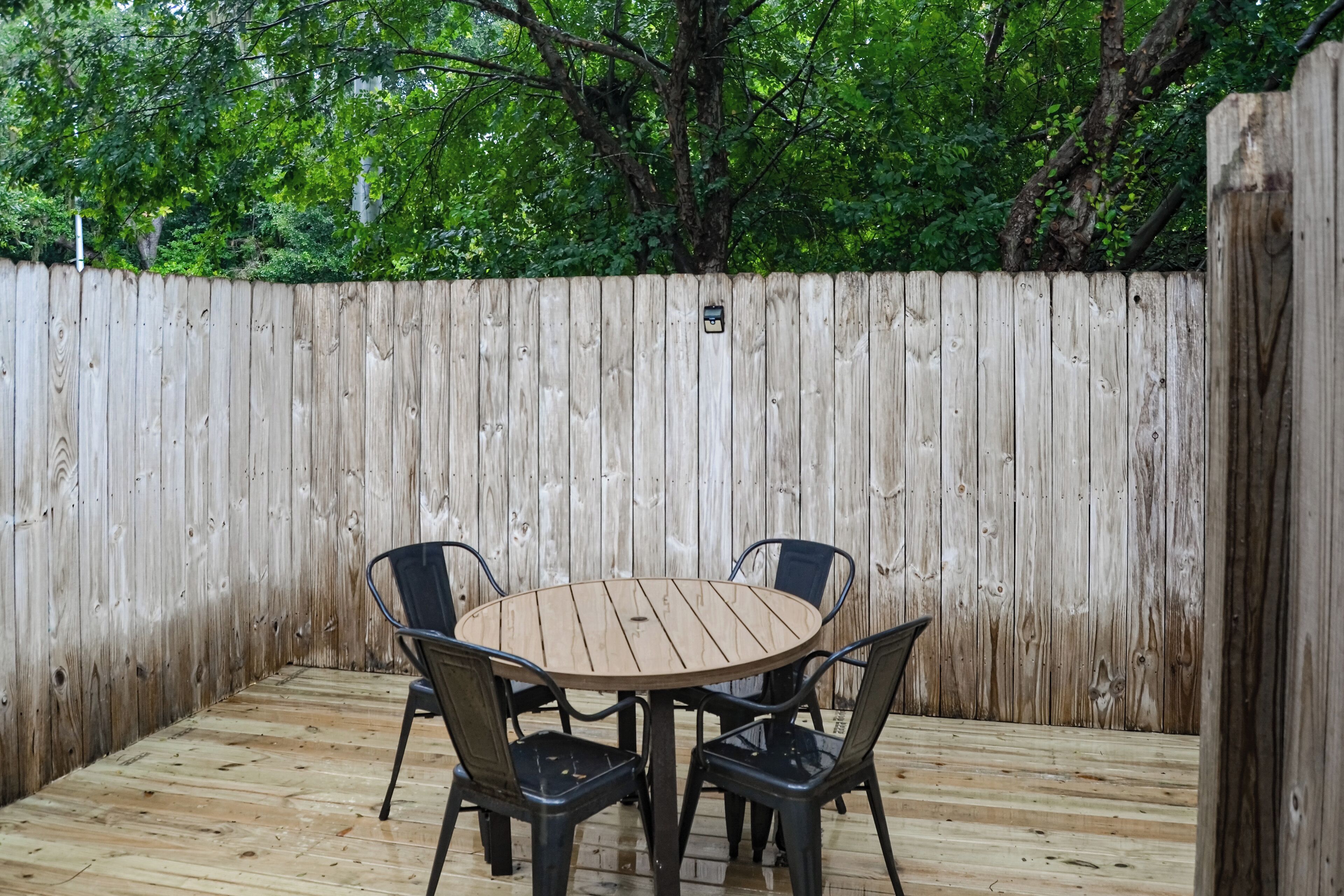 Una terraza exterior de madera con una mesa redonda y cuatro sillas.