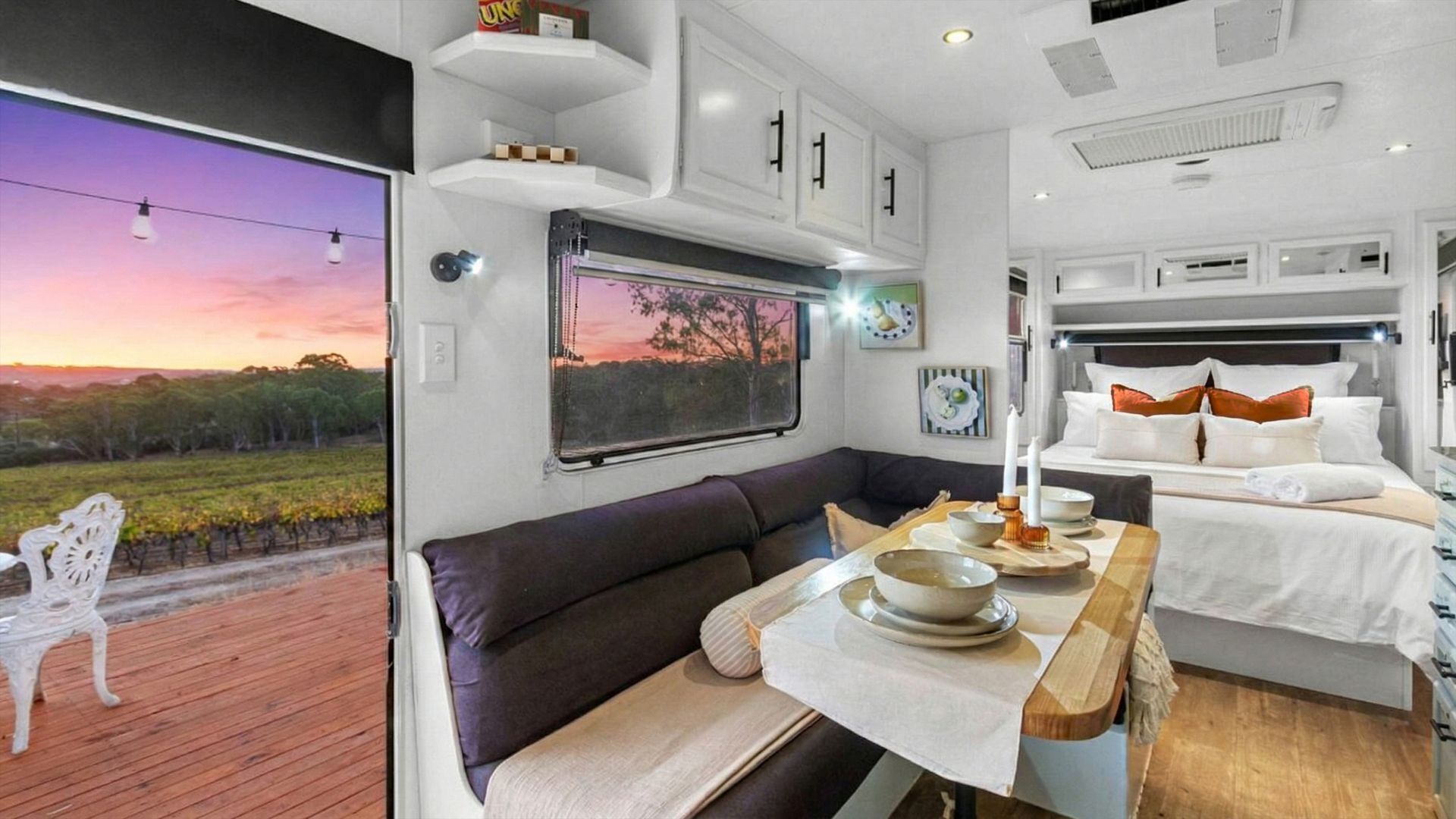 Interni moderni di un camper con zona pranzo, divano, letto e una vista panoramica dalla finestra.