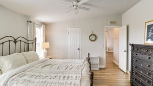 A bedroom with a bed, a dresser, a ceiling fan, a door, and a hallway leading to another room. - Scenic Sandia Mtn Views! Cozy Rio Rancho Retreat (Rio Rancho)