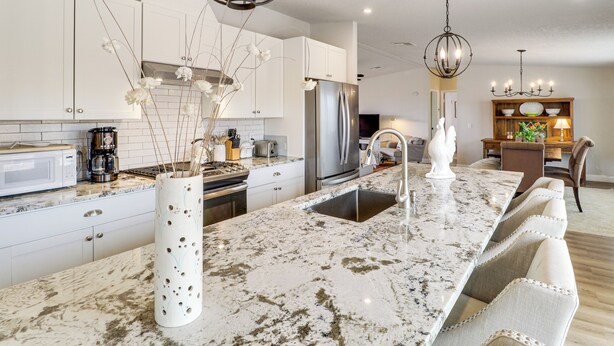A modern kitchen with white cabinets, a large marble island, stainless steel appliances, and a dining area with a wooden table and chairs. - Scenic Sandia Mtn Views! Cozy Rio Rancho Retreat (Rio Rancho)