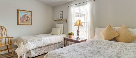 A bedroom with two beds, a wooden chair, a bedside table with a lamp, and a window with curtains.