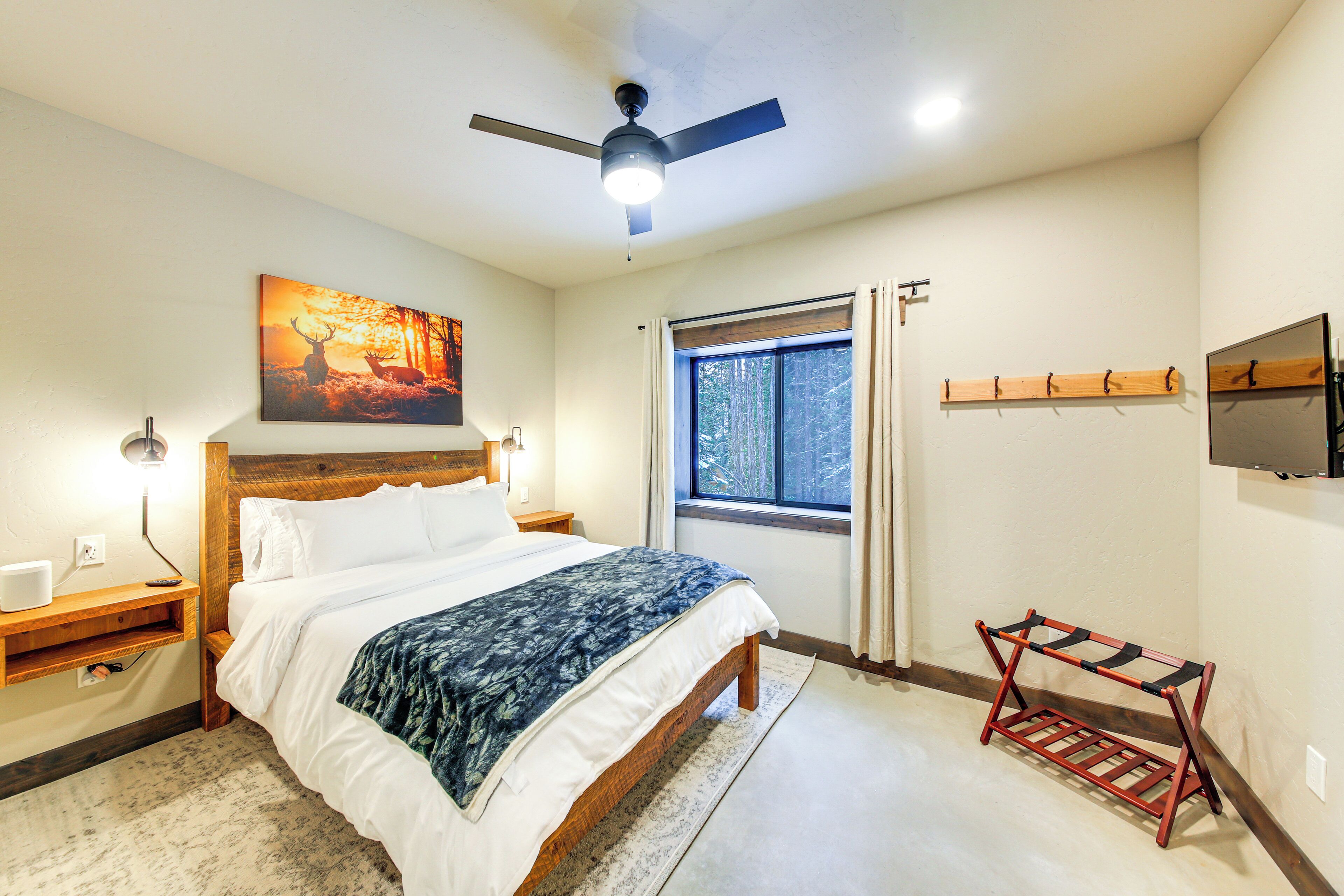 A bedroom with a bed, a ceiling fan, a window with curtains, a mounted TV, and a wooden shelf.