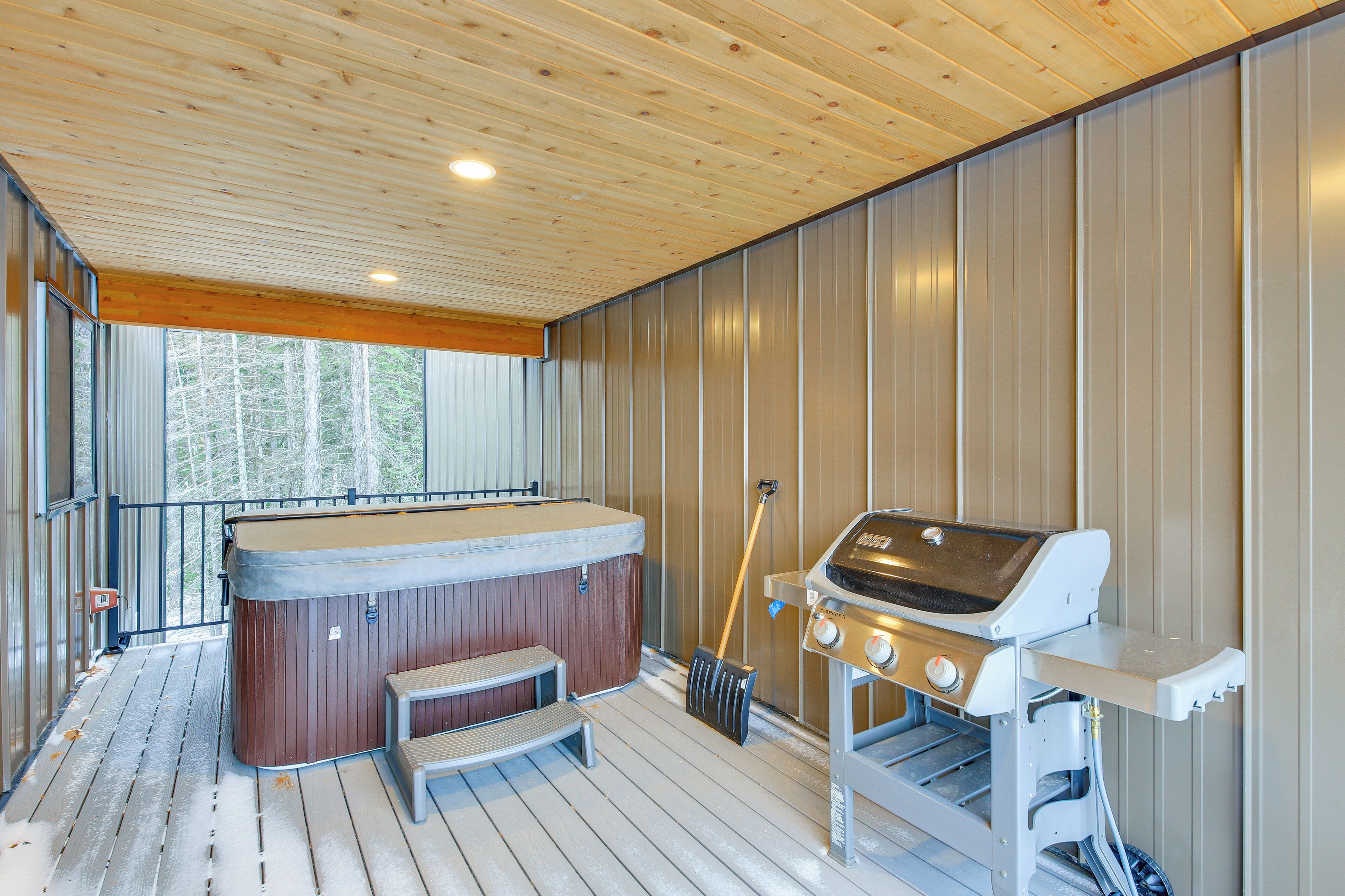 A wooden deck with a hot tub, a grill, and a bench.