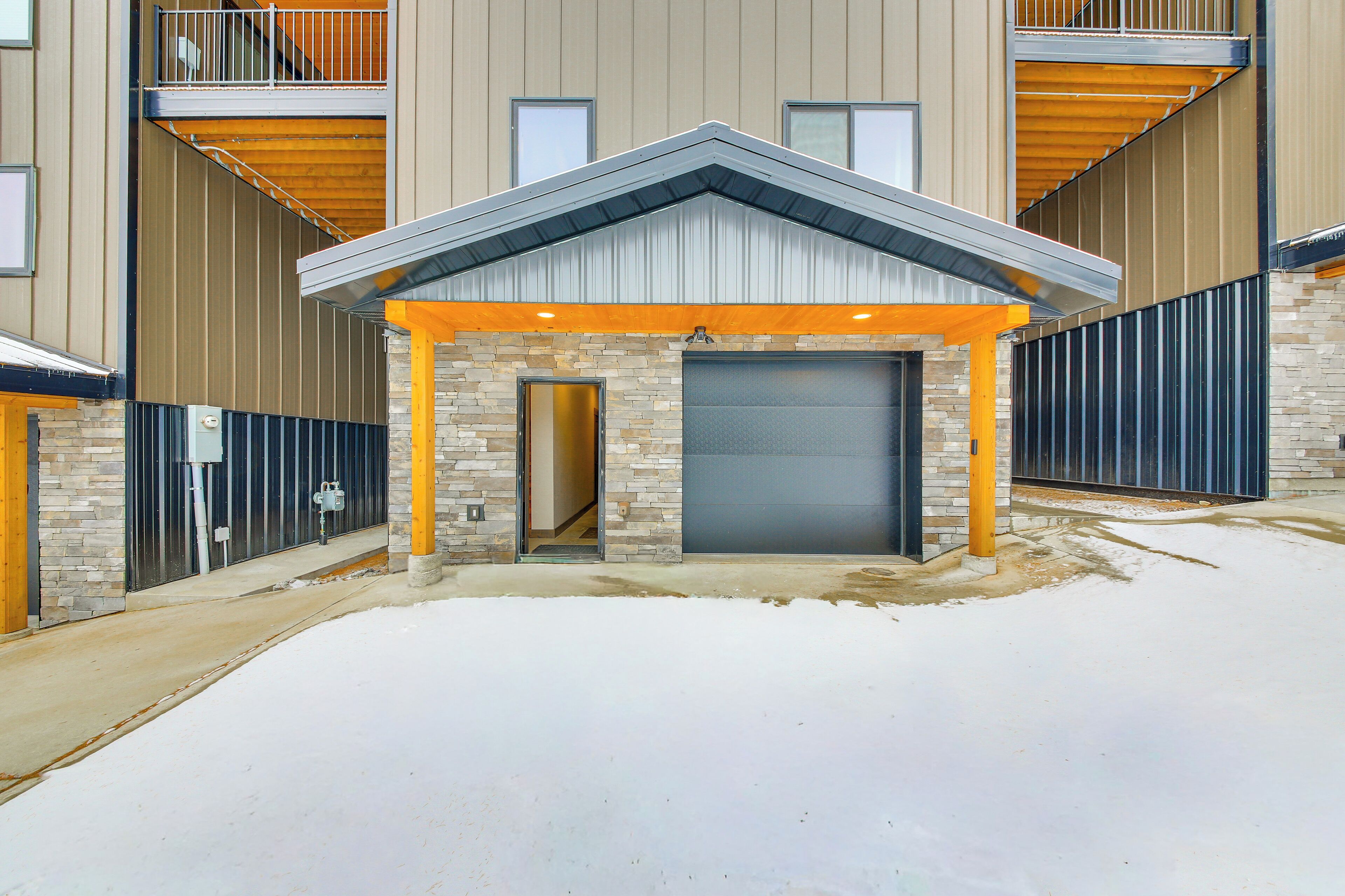 Un bâtiment moderne doté d’une entrée de garage, d’une façade en pierre et d’un espace couvert avec un toit en métal.