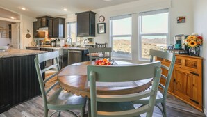A kitchen with dark cabinets, a wooden dining table, and a view of the desert through large windows. - Mtn Views, 15 Mi to Dtwn Kingman: Family Home! (Kingman)