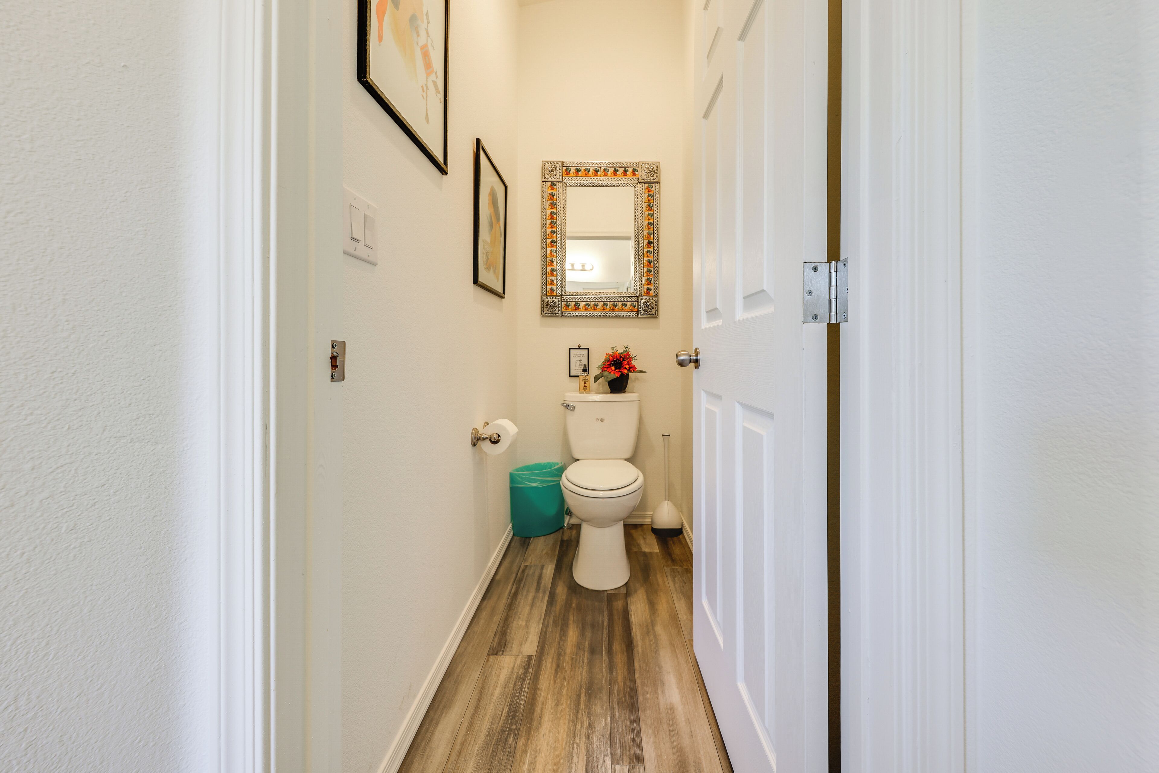 A narrow hallway leading to a bathroom with a toilet, a mirror, and a trash bin.