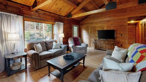 Interior acogedor de una cabaña con techo de madera, un conjunto de sofás, un televisor y una ventana con cortinas.
