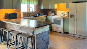 Una cocina con armarios de madera, una isla central con taburetes, un refrigerador y una estufa.