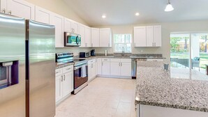 A modern kitchen with white cabinets, stainless steel appliances, granite countertops, and a large window providing natural light. - A Place in the Sun: Close to Shops & Attractions (Ocala)