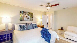 A bedroom with a large bed, a ceiling fan, a painting, a nightstand, a chair, and a door. - A Place in the Sun: Close to Shops & Attractions (Ocala)