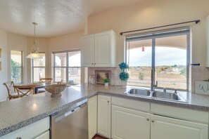 A kitchen with white cabinets, a granite countertop, a dishwasher, and a window with a view of the outside.