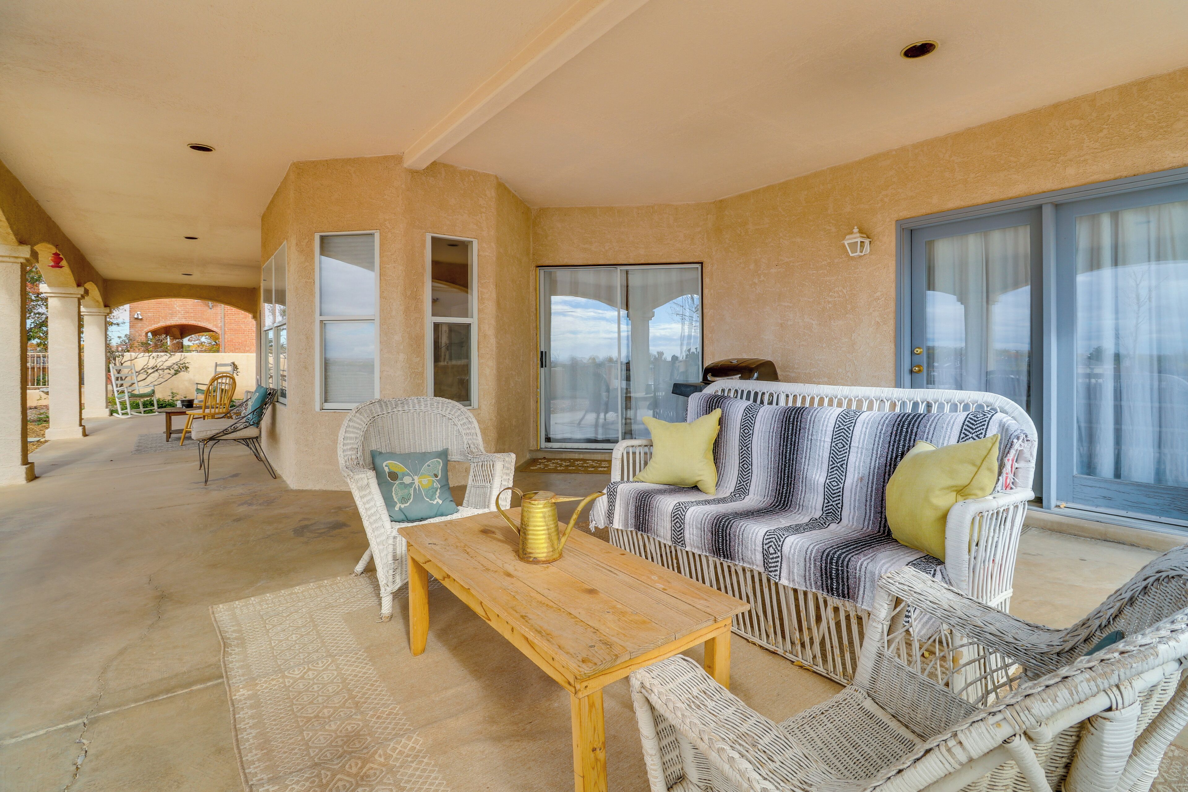 A covered patio area with wicker furniture, a wooden table, and a sliding glass door leading to an outdoor space.