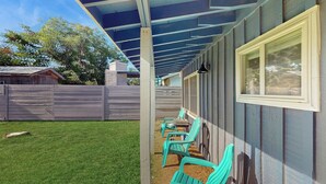 A covered patio area with green chairs and a table, a wooden fence, and a building with a window. - Wine Country Retreat w/ Yard: 1 Mi to Main Street (Fredericksburg)