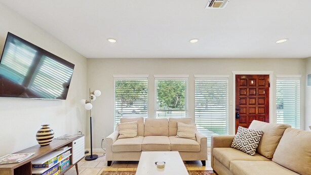 A living room with a beige sofa, a coffee table, a TV mounted on the wall, and a bookshelf with books. - Wine Country Retreat w/ Yard: 1 Mi to Main Street (Fredericksburg)