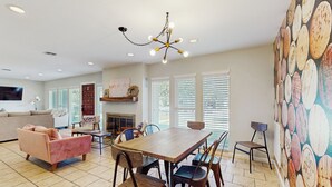 A spacious living room with a wooden dining table, comfortable seating, a fireplace, and large windows. - Wine Country Retreat w/ Yard: 1 Mi to Main Street (Fredericksburg)
