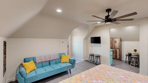 A bedroom with a bed, a blue sofa, a ceiling fan, and a kitchenette area. - 'lone Star Leisure' Condo w/ Hill Country Views (Fredericksburg)