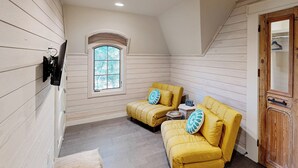 A corner room with two yellow sofas, a small table, a window with a view, and a wooden door. - 'lone Star Leisure' Condo w/ Hill Country Views (Fredericksburg)