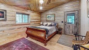 Un dormitorio de cabaña de madera con una cama de madera, una silla, una alfombra y una puerta con ventanal.