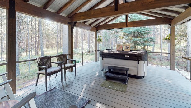 Una terraza techada al aire libre con vigas de madera, una parrilla, dos sillas y un felpudo.