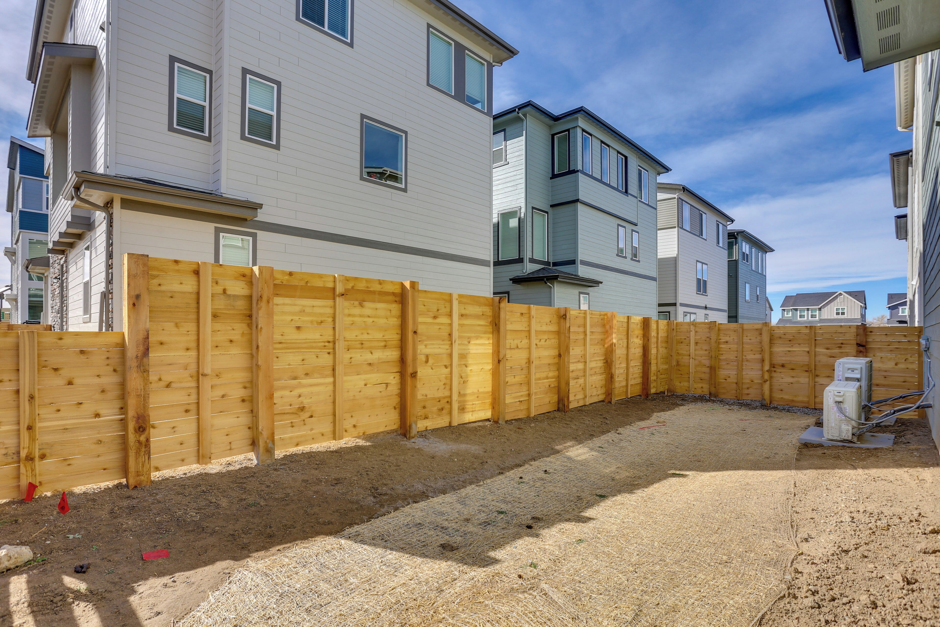 Quartiere residenziale con recinzione in legno, case e cielo sereno.