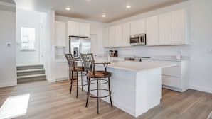 A modern kitchen with white cabinetry, a central island with stools, a stainless steel refrigerator, and a microwave. - 8 Mi to Denver Tech Center: Business-ready Retreat (Centennial)
