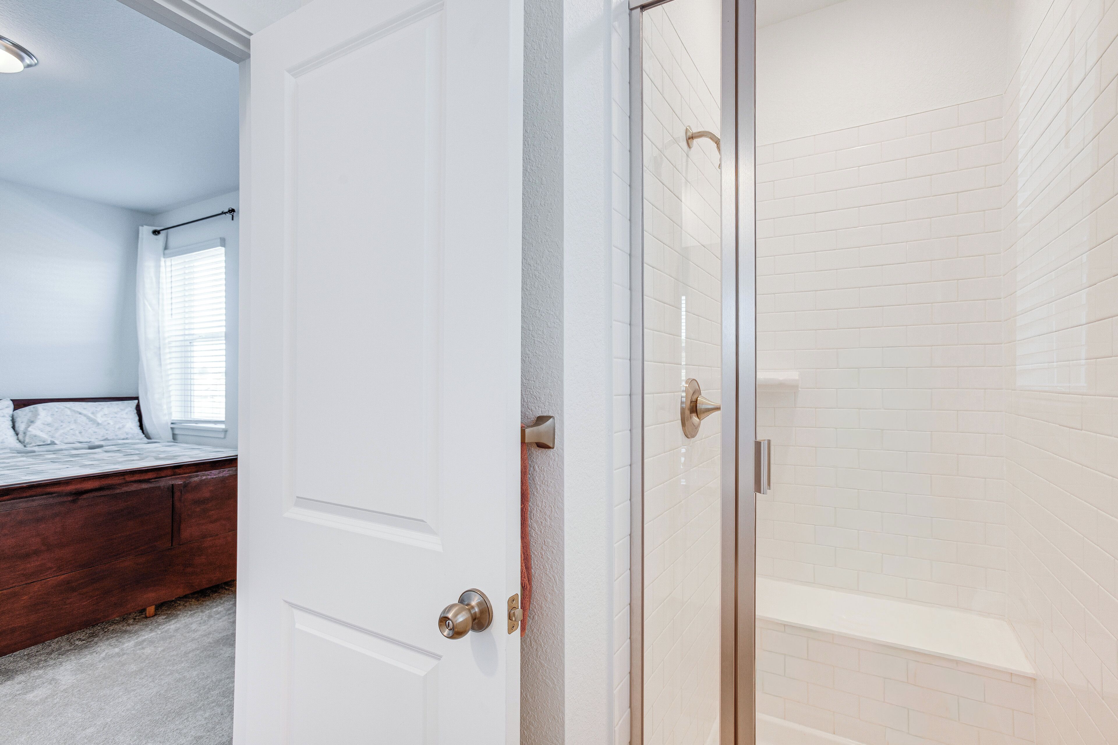 A bedroom with a wooden bed, a white door, and a shower area with white tiles.