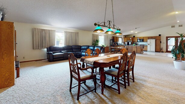 A spacious living room with a dark leather sofa, a wooden dining table with chairs, and a kitchen in the background.