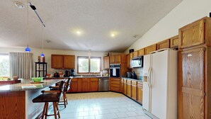 A spacious kitchen with wooden cabinets, a central island with bar stools, a refrigerator, and a microwave.