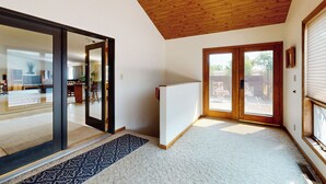A spacious room with a large sliding glass door leading to an outdoor area, a wooden ceiling, and a patterned rug.