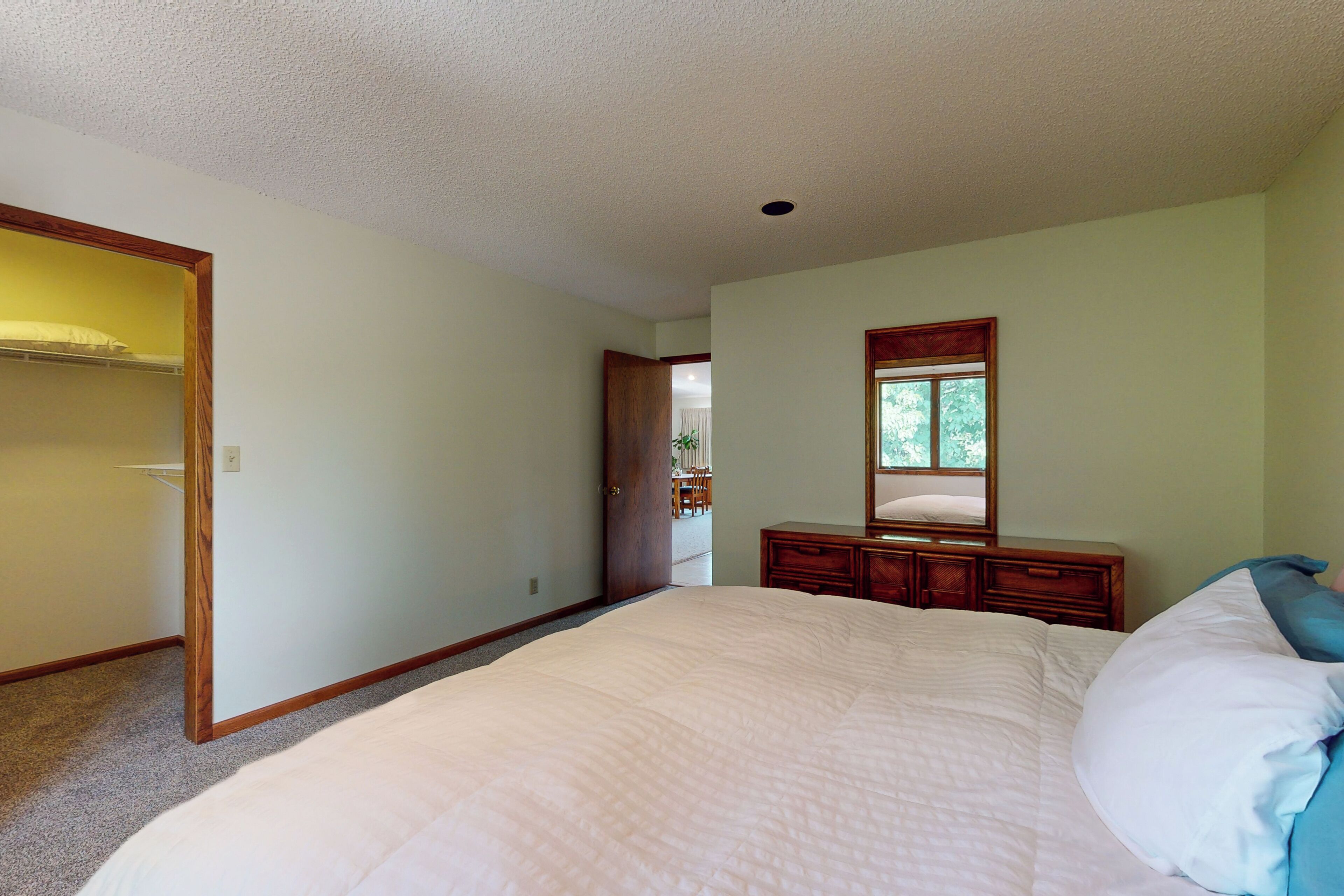 A bedroom with a large bed, a dresser, a mirror, and a closet.