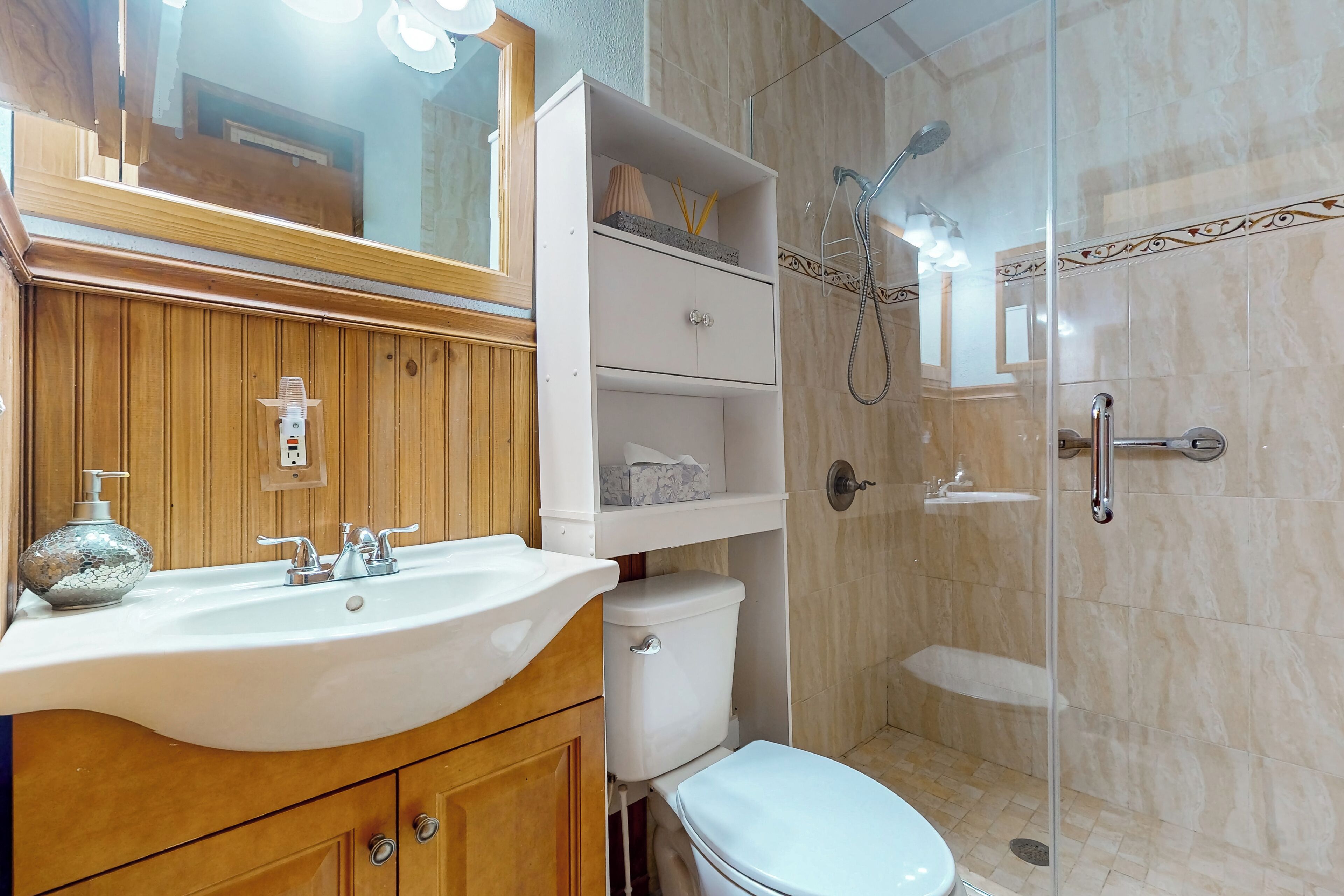 A bathroom with a wooden vanity, white sink, and a glass-enclosed shower.