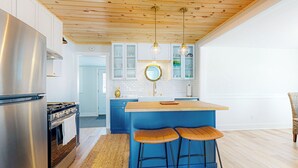 A modern kitchen with a wooden ceiling, stainless steel appliances, and blue bar stools. - Walk to Downtown & Beach! Water-view Home (East Tawas)