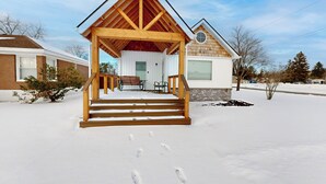 A wooden cabin with a porch and steps leading to a door. - Walk to Downtown & Beach! Water-view Home (East Tawas)