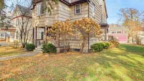 A two-story house with a front porch, a small tree with yellow leaves, and a lawn covered with fallen leaves. - Central Duplex Townhome Close to Twin Cities (St. Paul)
